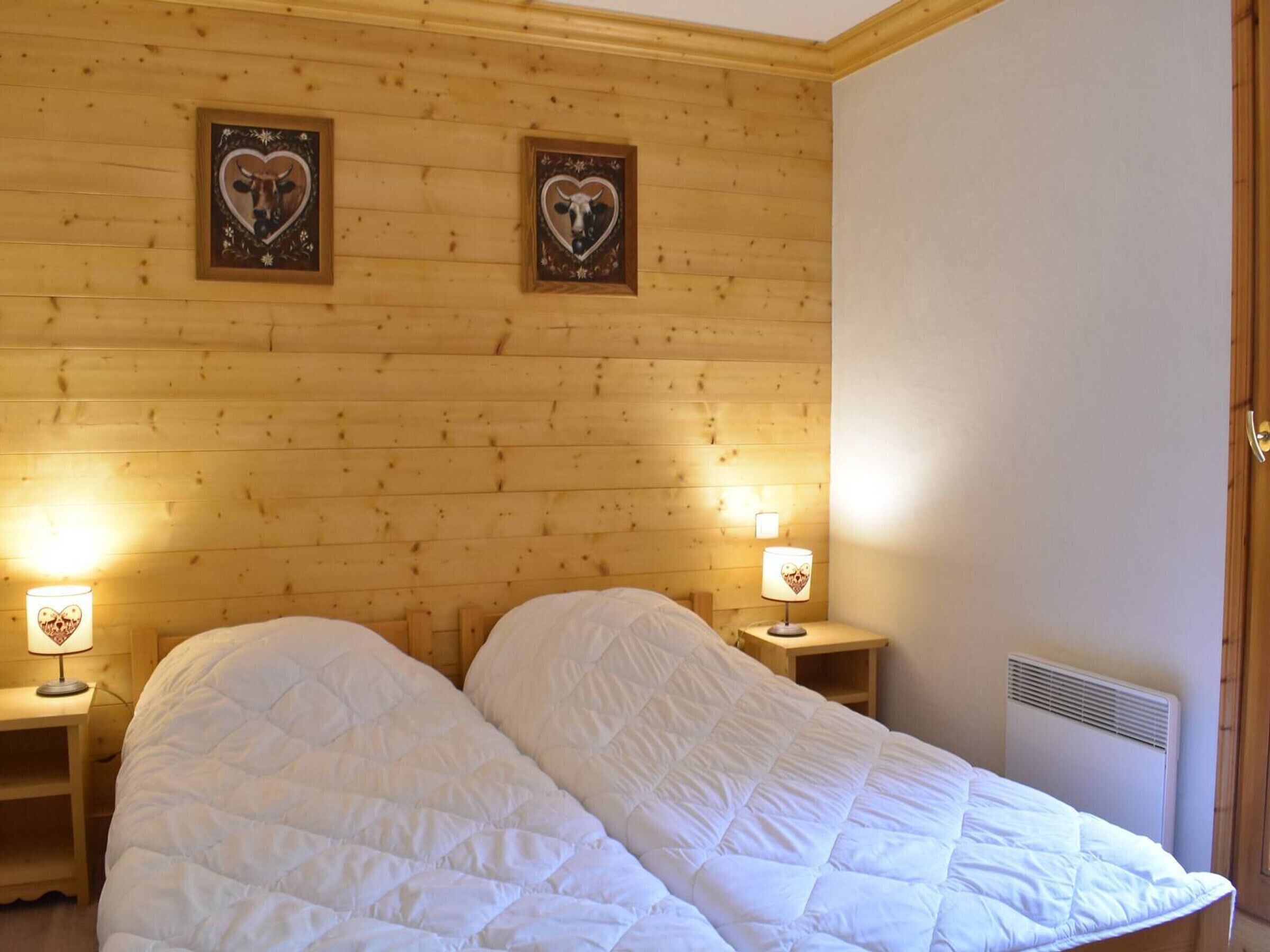 A room with wooden panel walls, two beds with white quilts, and two bedside lamps with heart-shaped lampshades.