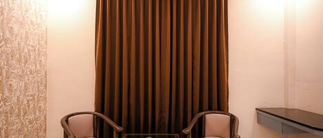 A room with two wooden chairs, a small table, and a brown curtain.