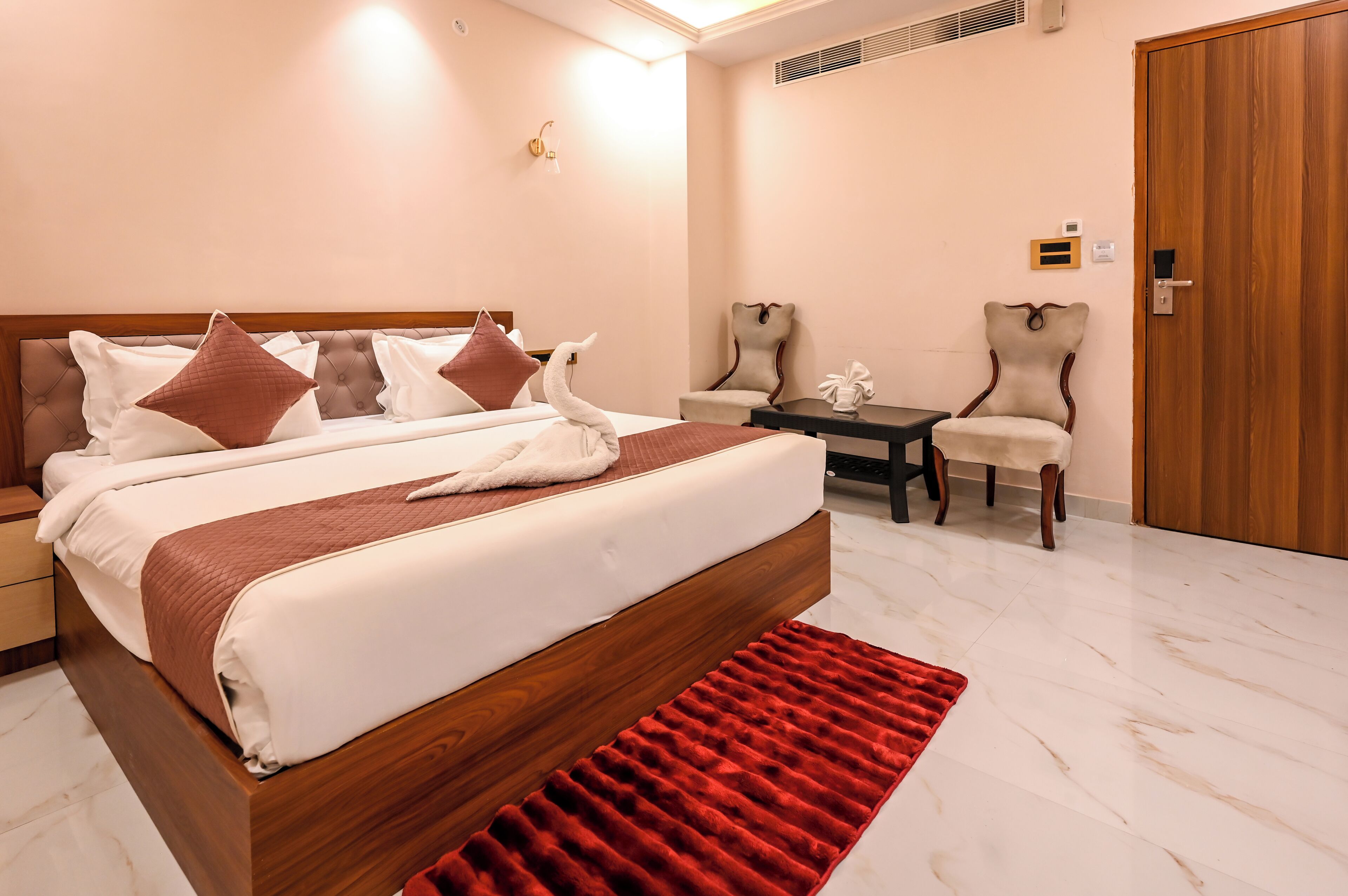 Une chambre d’hôtel avec un grand lit, deux chaises, une petite table et une armoire en bois.