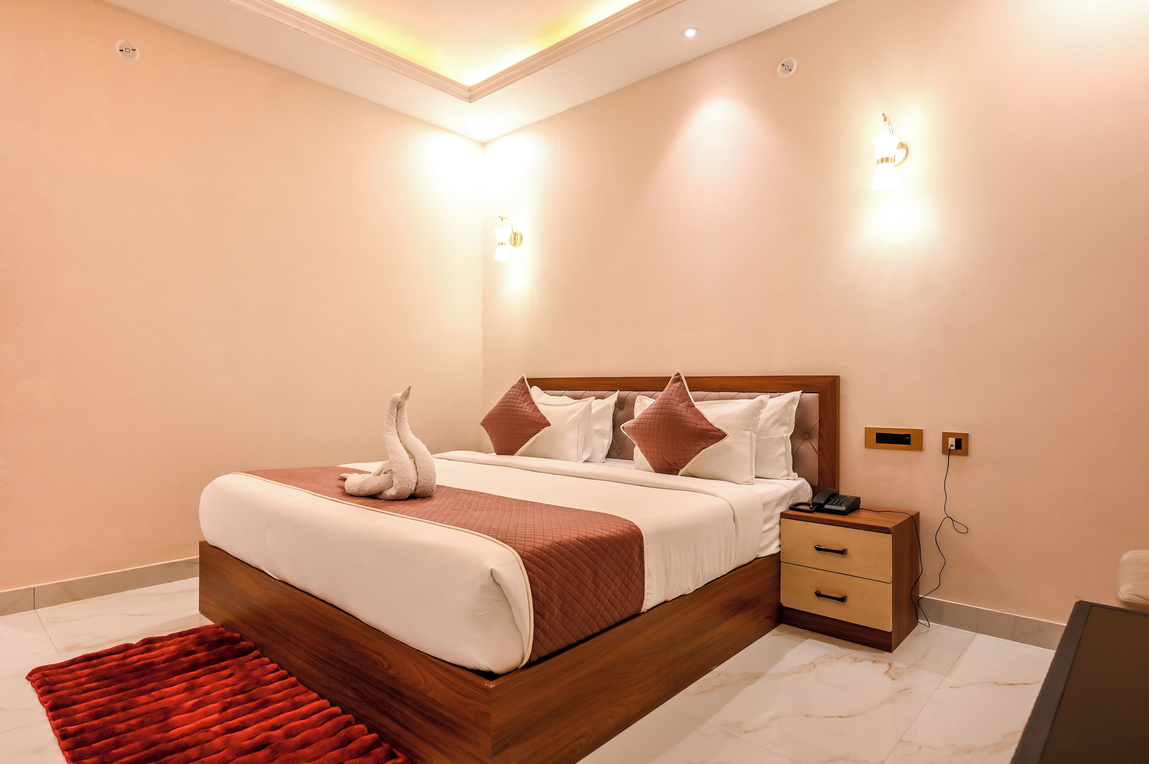 A modern bedroom with a wooden bed frame, a red rug, a bedside table, and a wall-mounted light fixture.