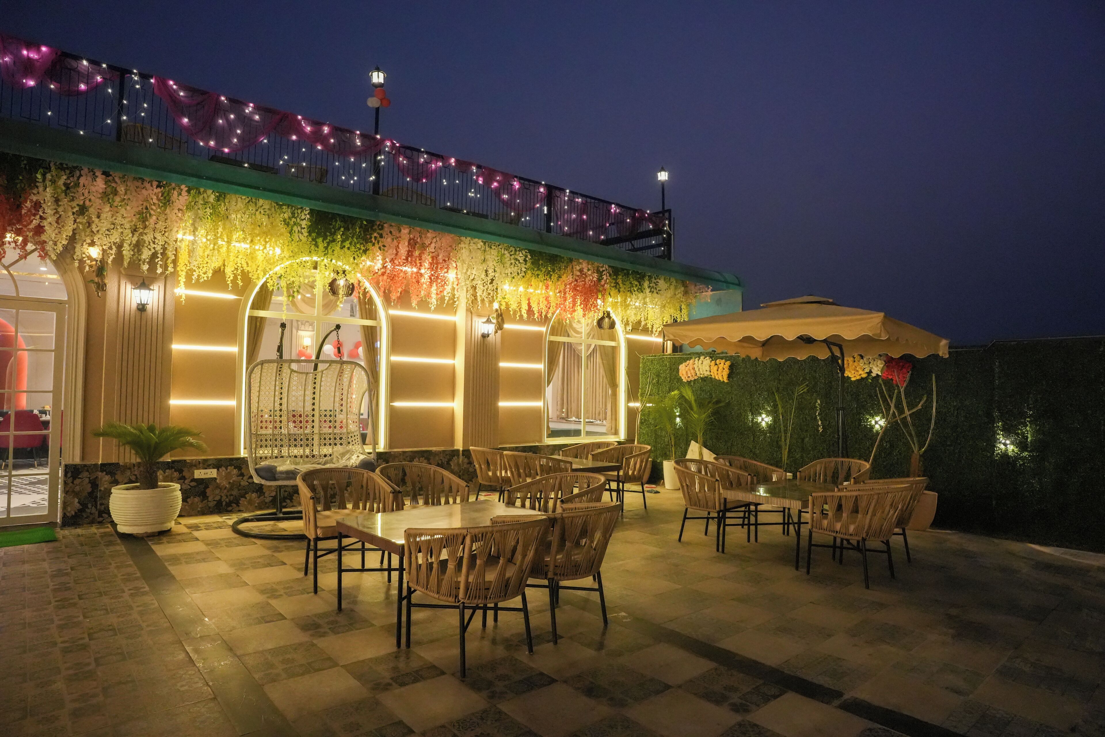 Un espace extérieur aménagé avec des tables et des chaises, une partie couverte avec un auvent, et un balcon décoré de guirlandes lumineuses.