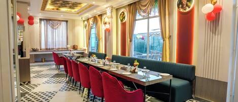 A dining area with a long table, red chairs, and a green sofa.