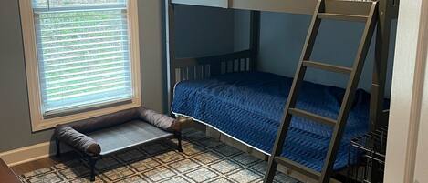 A bunk bed room with a window, a bench, and a patterned rug.