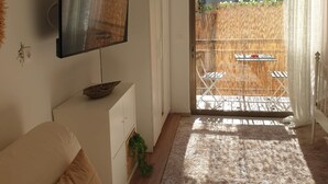 Una sala de estar acogedora con una televisión de pantalla plana, un sofá y un ventanal corredizo que da a un espacio exterior con cerca de bambú y una mesa.