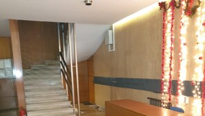Una zona de recepción con un mostrador de madera, una escalera al fondo y un extintor de incendios en el suelo.