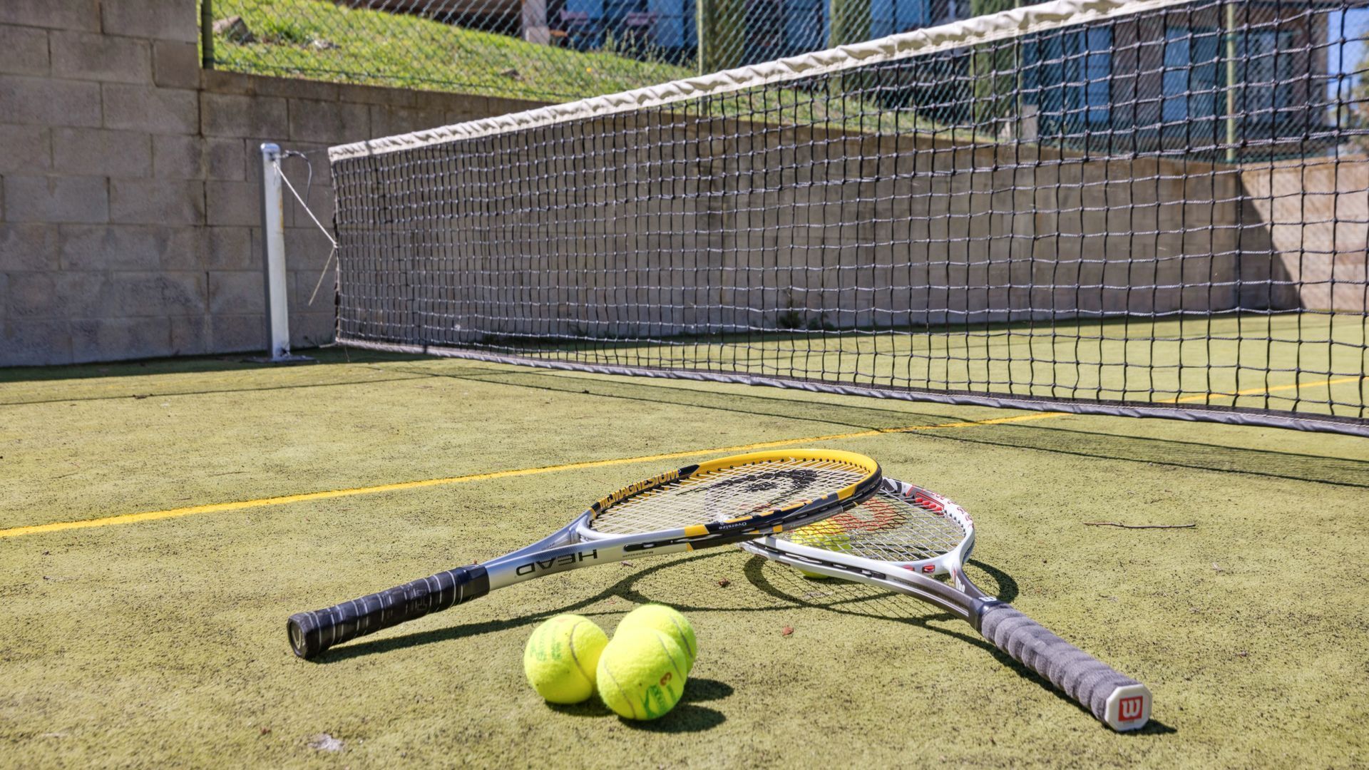 A tennis court with a net, two tennis rackets, and three tennis balls.