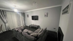 Una sala de estar con un sofá modular, un televisor de pantalla plana, una mesa con un florero y una araña.