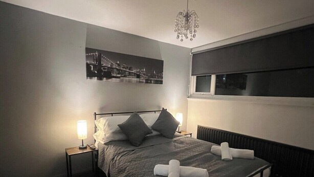 Un dormitorio moderno con una cama grande, dos lámparas de noche, una araña y una obra de arte con una vista urbana en la pared.