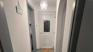 Un pasillo estrecho con suelo de madera, paredes blancas y una puerta con un panel de vidrio.