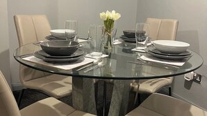 Una mesa redonda de vidrio con cuatro sillas color beige, un florero con flores blancas y una decoración en forma de corazón en la pared.