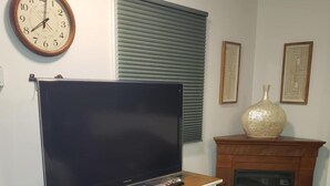 A living room with a flat-screen TV on a wooden stand, a fireplace, a clock, and two framed artworks on the wall. - 1 Mile From Ski Slope and Festivals - 125 Nightly Fee (Hunter)