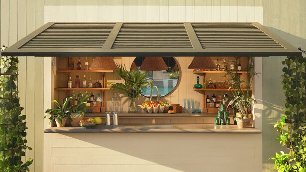 A bar area with a wooden counter, shelves with bottles, and potted plants. - The Maidstone New Orleans (New Orleans)