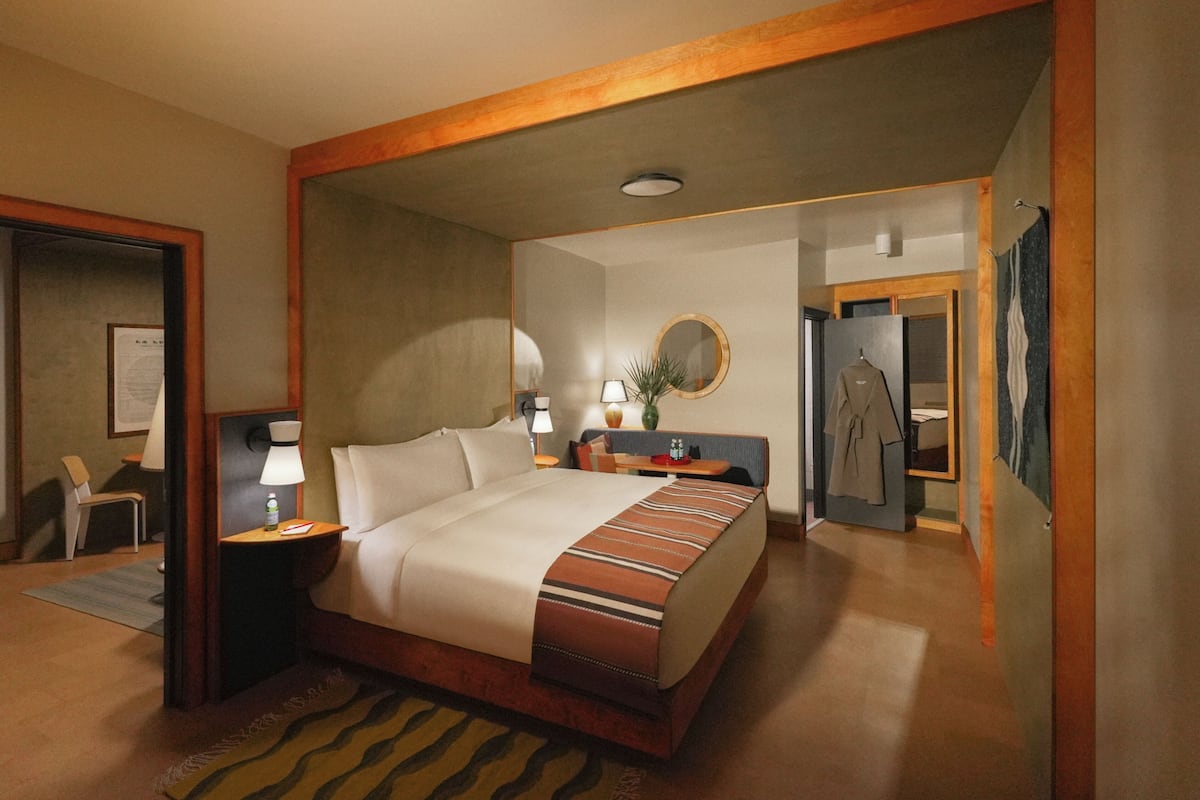 Een hotelkamer met een groot bed, nachtkastjes, een spiegel, een kapstok en een deur naar een andere kamer.