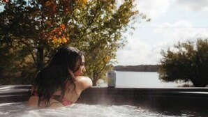 Une personne dans un bain à remous, avec vue sur un lac et des arbres en arrière-plan.