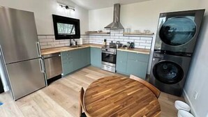 Une cuisine moderne équipée d’appareils électroménagers en acier inoxydable, d’une table à manger en bois, ainsi que d’un lave-linge et d’un sèche-linge intégrés.