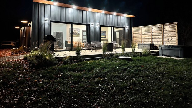 Une maison moderne dotée d’une grande porte vitrée, d’un espace salon extérieur et d’un coin barbecue.