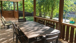 Une terrasse extérieure avec une table et des chaises en bois, entourée d’une balustrade en bois et d’arbres.
