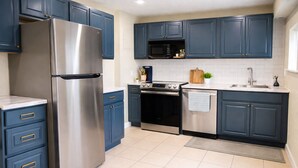 Une cuisine avec des meubles de couleur bleu foncé, des appareils électroménagers en acier inoxydable et un sol carrelé.