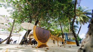 Eine Strandkulisse mit einer großen Holzskulptur, Palmen und Sitzgelegenheiten im Freien.