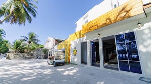 A building with a yellow and white facade, a parked golf cart, and palm trees in the background. - VelaaVani - Turtle Hive Dhiffushi (Dhiffushi)
