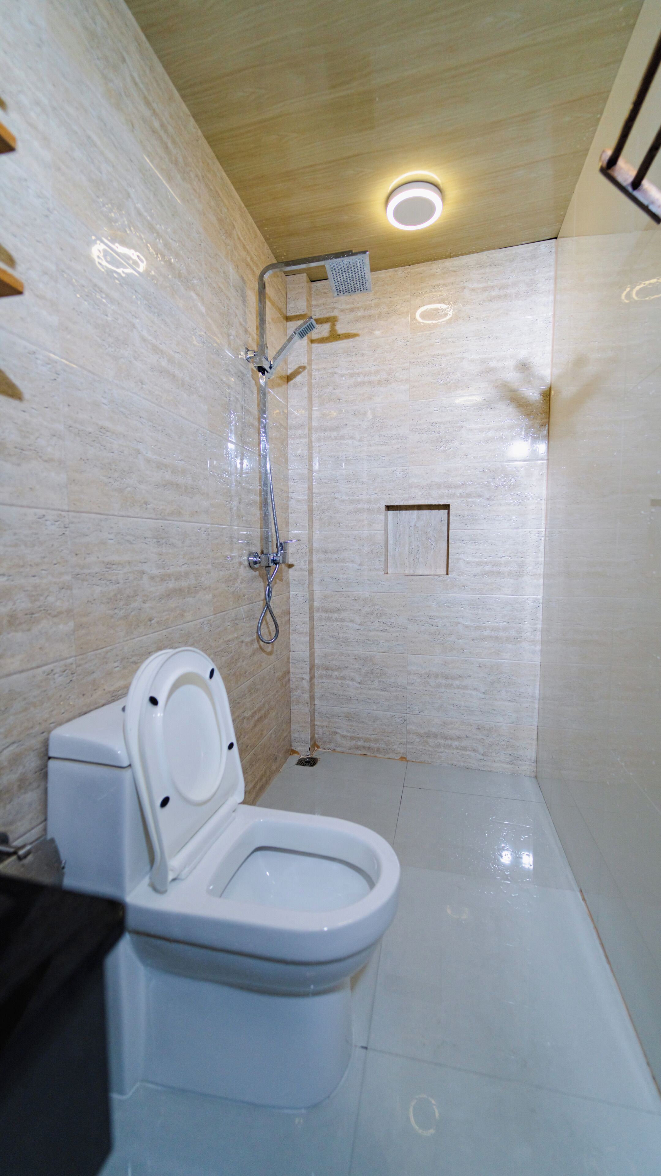 Un baño con inodoro, ducha y un pequeño estante de madera.