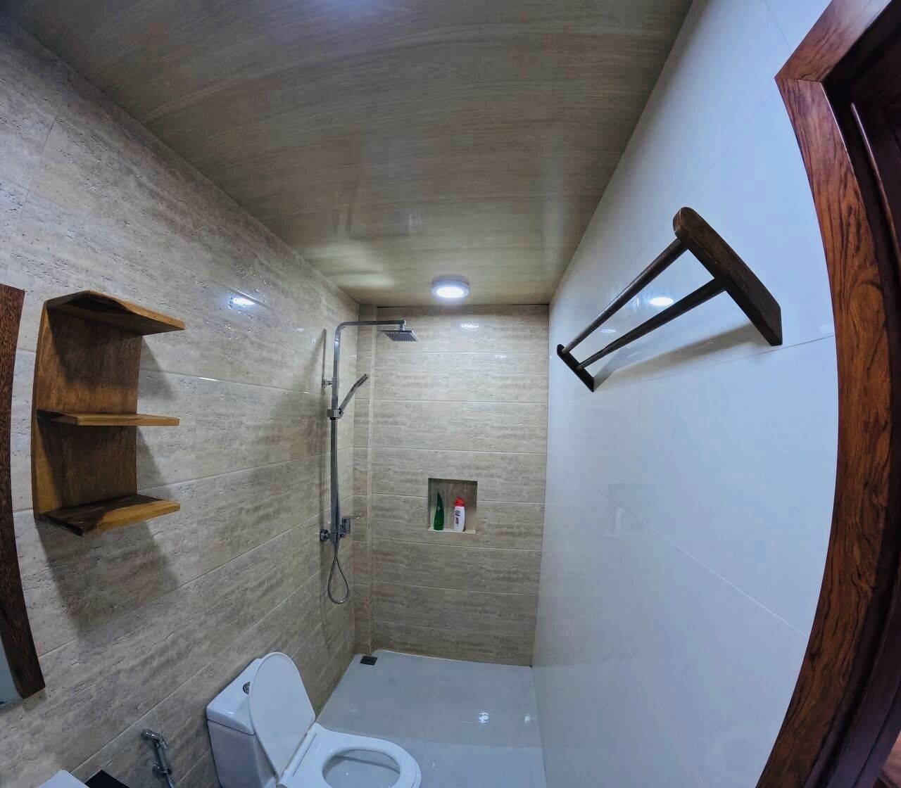 A compact bathroom with a shower, toilet, and a small shelf unit.