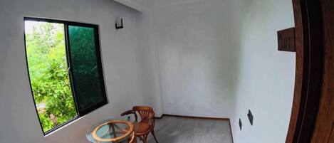 Ein Zimmer mit Deckenventilator, einem Fenster mit Blick auf Grünflächen und einem Essbereich mit Tisch und Stühlen.