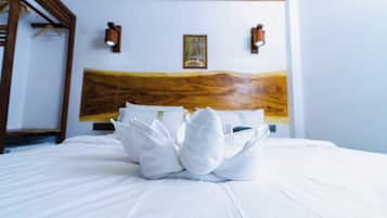 Ein ordentlich bezogenes Bett mit einer Handtuchgestaltung in der Mitte, ein Holz-Kopfteil und zwei an der Wand befestigte Lampen.