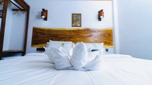 Una cama bien hecha con un arreglo de toallas en el centro, un cabecero de madera y dos luces fijadas a la pared.