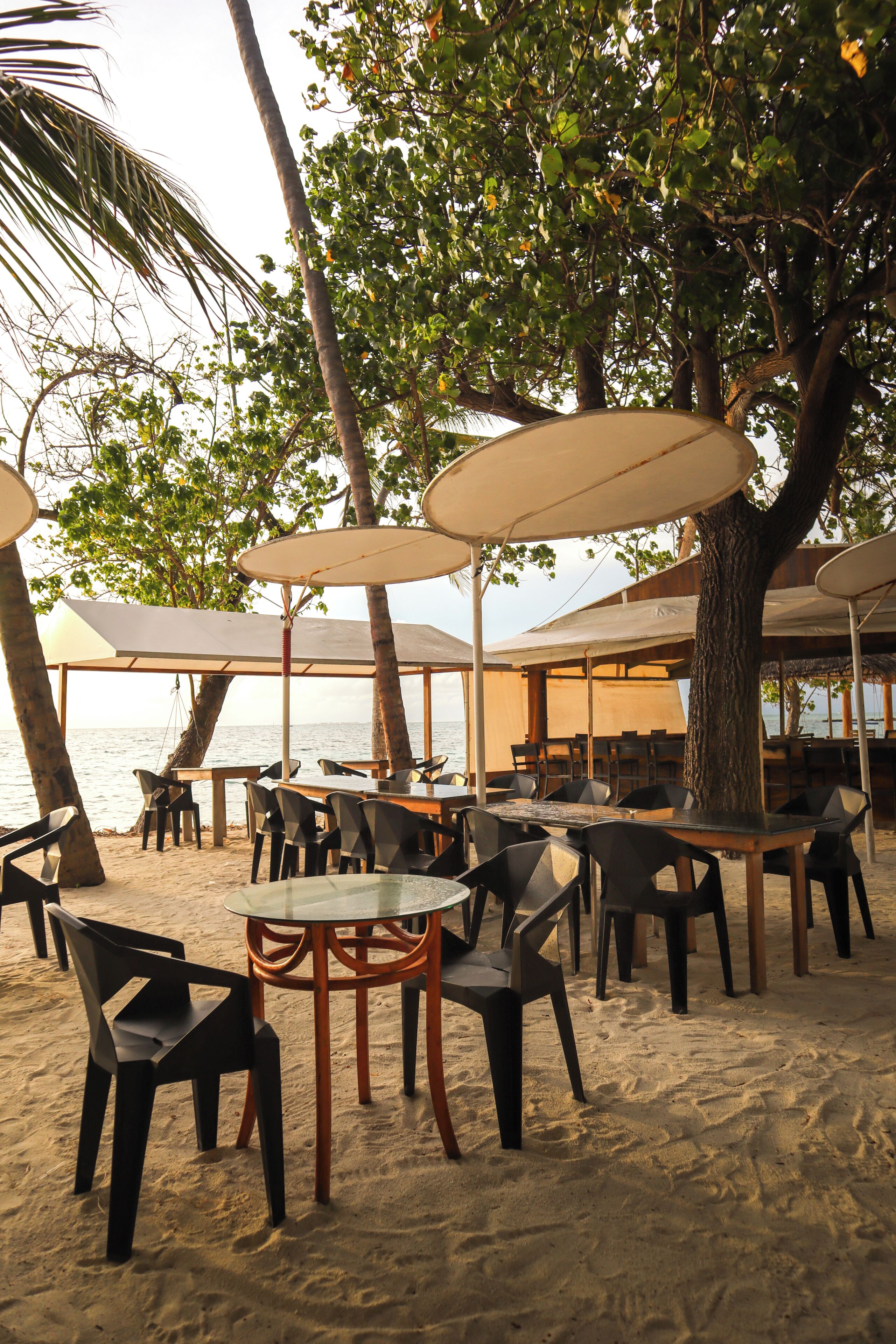 Terrasse mit Tischen und Stühlen, Sonnenschirmen und Strandambiente.