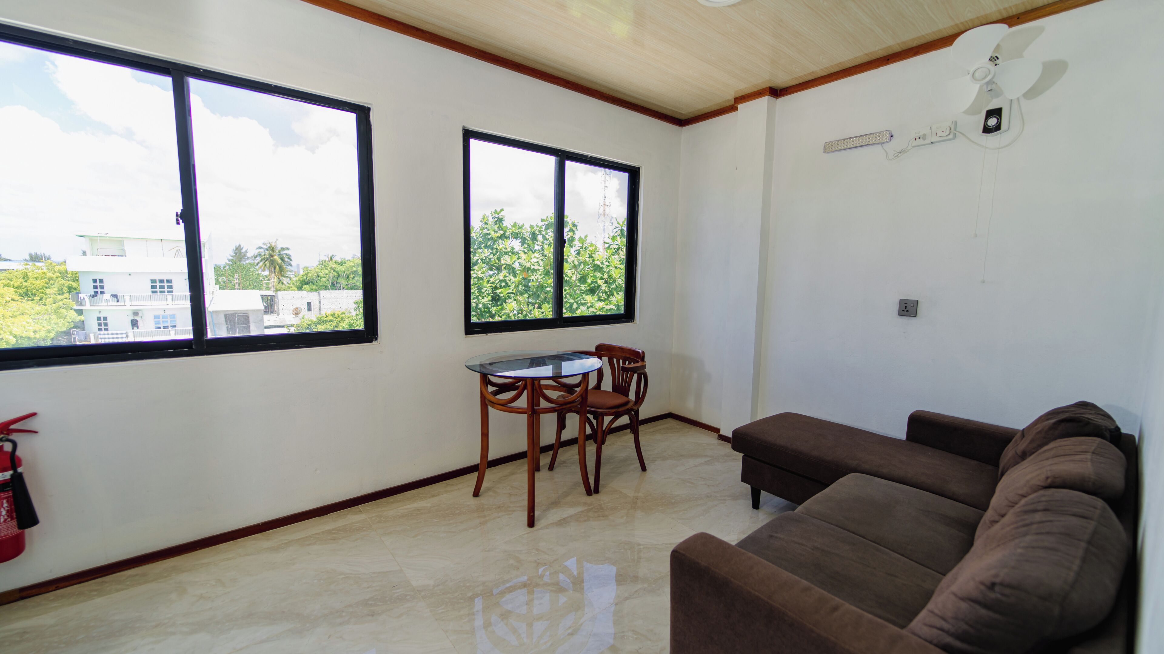 Una habitación con un sofá marrón, una pequeña mesa con sillas y dos ventanas.