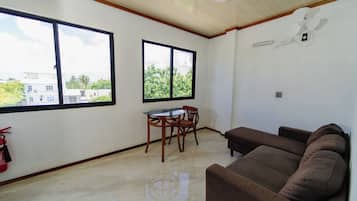 Una habitación con un sofá marrón, una pequeña mesa con sillas y dos ventanas.