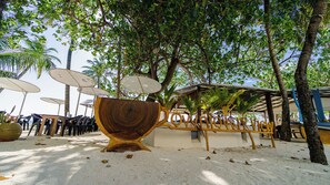 A beachside area with a wooden sculpture, umbrellas, and chairs. - VelaaVani - Turtle Hive Dhiffushi (Dhiffushi)