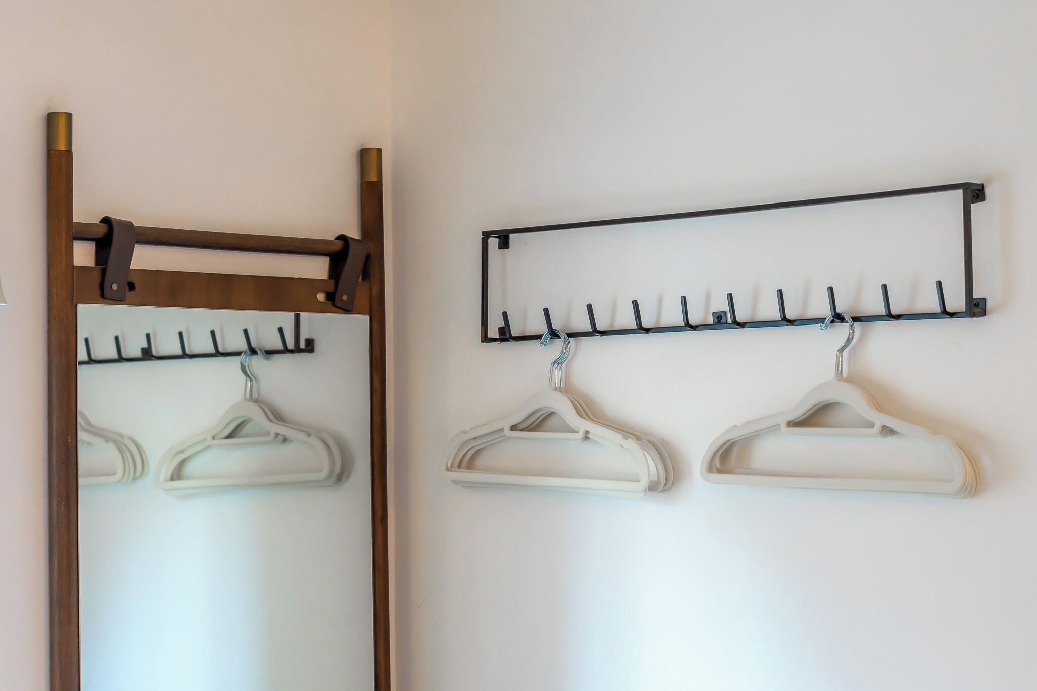 A wall-mounted coat rack with multiple hooks and two white hangers.