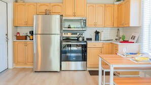 A compact kitchen with a refrigerator, oven, microwave, and wooden cabinets. - 1 BR Apt - Walk to Historic Hub (St. Augustine)