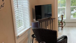 A dining area with a television on a stand, wicker chairs, and a table set with plates and glasses. - 1 BR Apt - Walk to Historic Hub (St. Augustine)