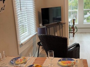 A dining area with a television on a stand, wicker chairs, and a table set with plates and glasses. - 1 BR Apt - Walk to Historic Hub (St. Augustine)