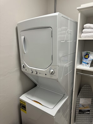 Eine Waschmaschine mit Frontlader, ein Regal mit gefalteten Handtüchern und eine Waschmittelbox.