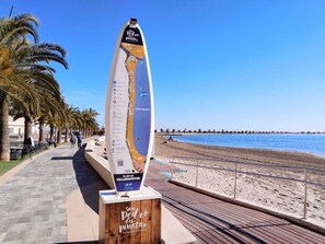 A tall, vertical sign with a map and text, located on a boardwalk by a beach with palm trees and a clear blue sky. - Al Alba Apartment (San Pedro del Pinatar)
