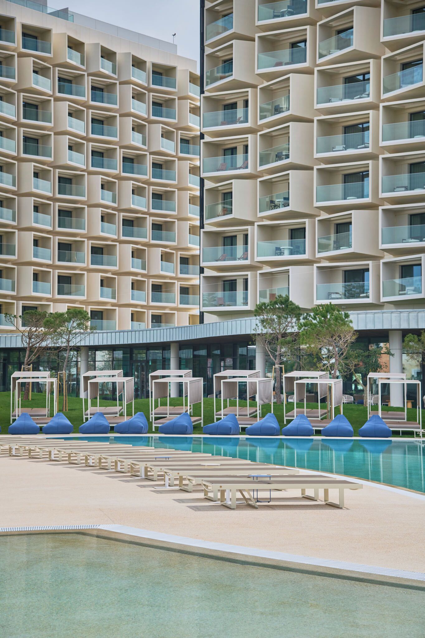 Un hotel moderno con zona de piscina, destacando una fachada geométrica y varios balcones.
