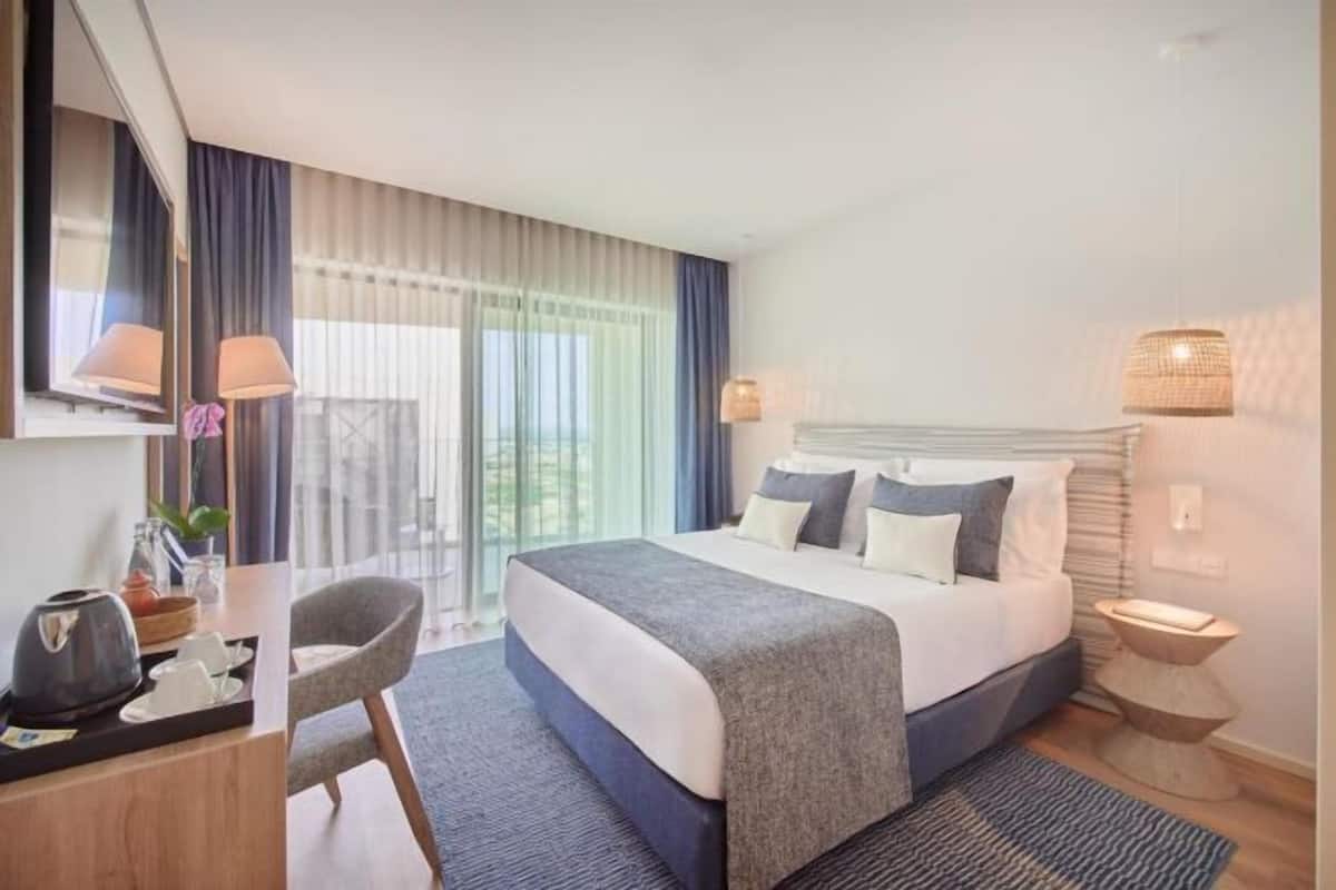 Ein Hotelzimmer mit einem großen Bett, einem Schreibtisch mit Stuhl, einem kleinen Tisch und einer Lampe.
