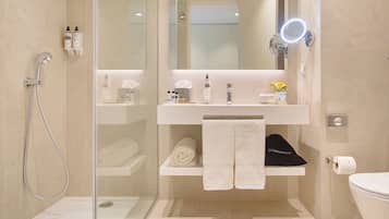 Un baño moderno con cabina de ducha de vidrio, lavamanos blanco con espejo y un inodoro.