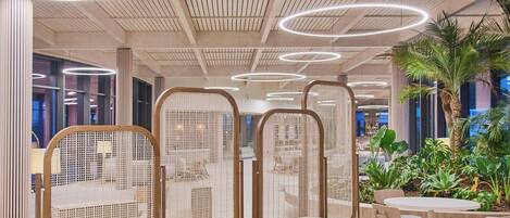Un interior moderno con una mesa redonda de madera y sillas, un techo con listones de madera y luces circulares, y vista a una palmera fuera.
