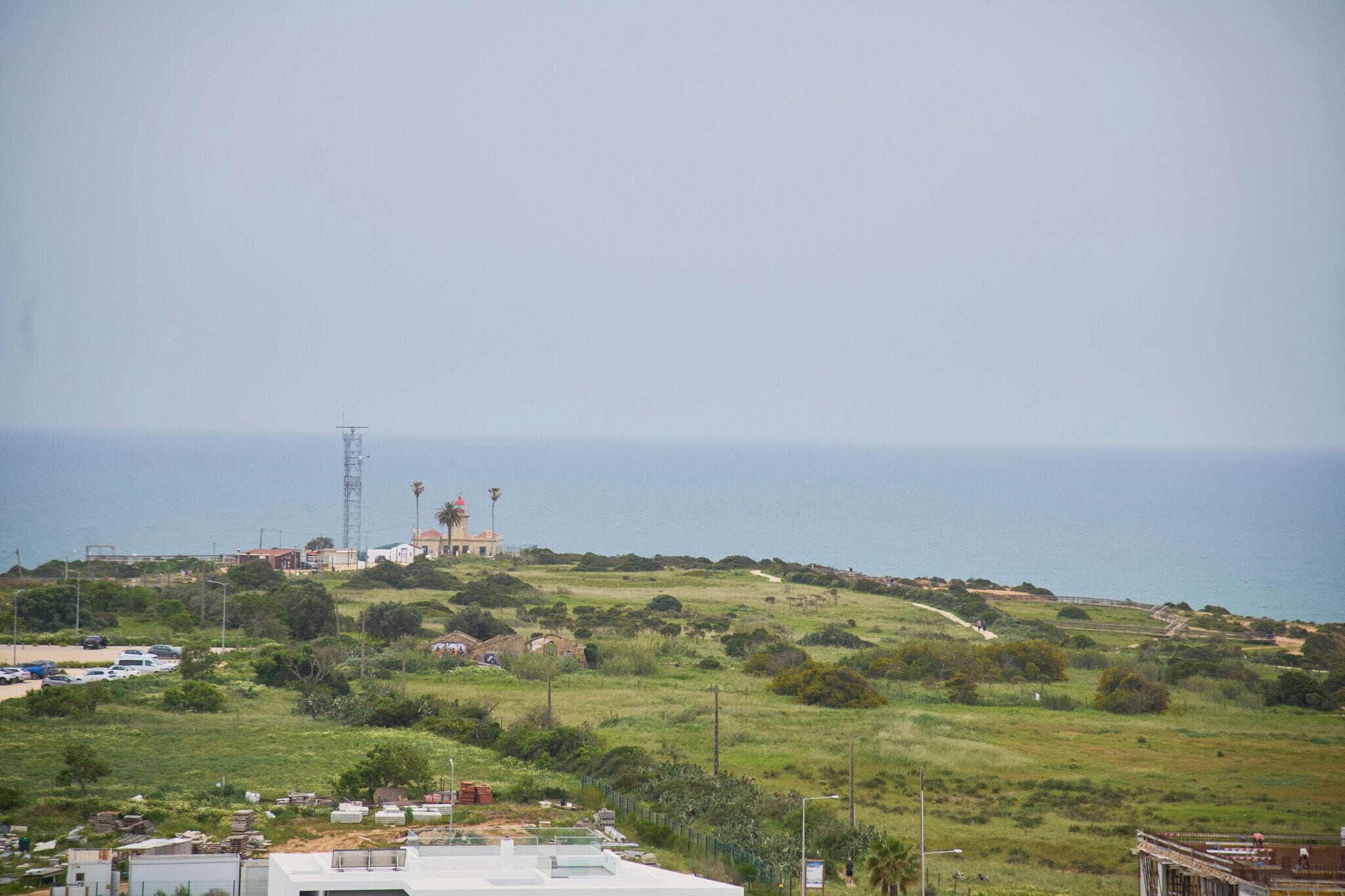 A coastal landscape with a lighthouse, a road, and scattered buildings.