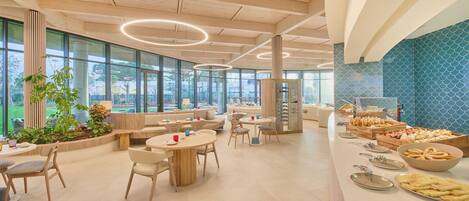 A modern cafe with round tables, chairs, and a buffet area with food items.