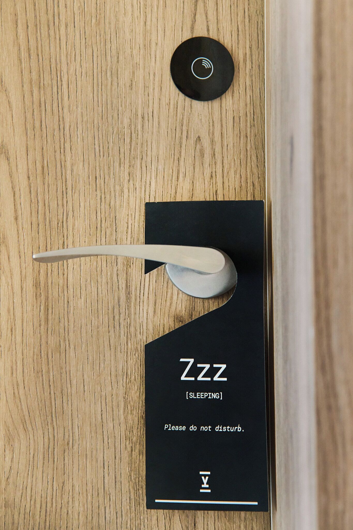 A modern door with a 'Zzz [SLEEPING]' sign and a polite request not to disturb.