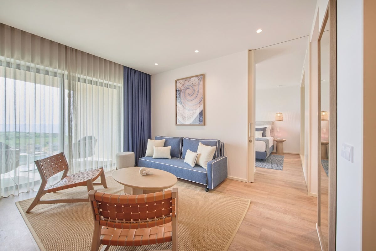 Ein modernes Wohnzimmer mit einem blauen Sofa, Holzstühlen, einem runden Tisch und einem großen Fenster mit transparenten Vorhängen.