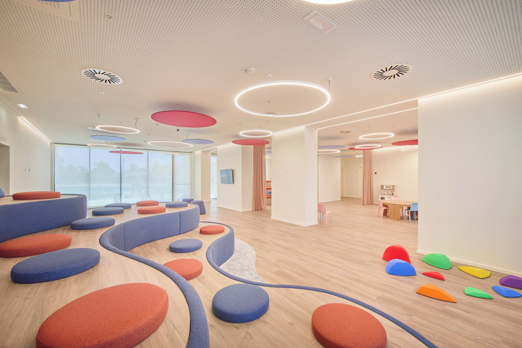 A modern interior with a wooden floor, colorful circular seating, and a ceiling with circular light fixtures.