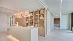 Ett modernt receptionsområde med en central ö, hyllor i trä med handdukar och hängande lampor i flätat material.