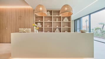 A reception desk with a neutral color scheme, two woven pendant lights, and a view of the outdoors through large windows.